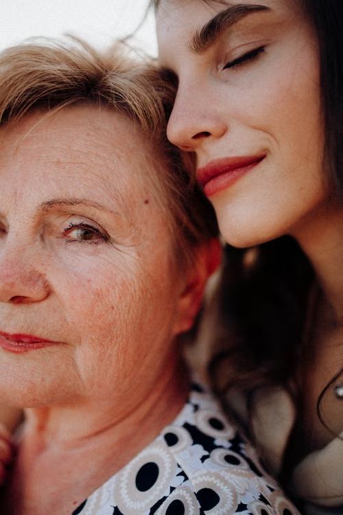 An adult daughter leaning affectionately against her mother